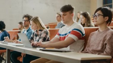 Yakışıklı beyaz öğrenci kullanır Laptop süre üniversitede ders dinleme. Çok etnik grup kendi gelecekte yatırım Modern parlak öğrenci.