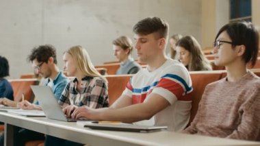 Yakışıklı beyaz öğrenci kullanır bir soru Üniversitesi, o el yükseltir ve öğretim görevlisi sorar bir ders dinlerken Laptop. Çok etnik grup Modern parlak öğrenci.