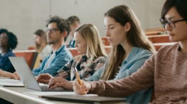 Güzel genç öğrenci kullanır bir soru Üniversitesi, o el yükseltir ve öğretim görevlisi sorar bir ders dinlerken Laptop. Çok etnik grup Modern parlak öğrenci.