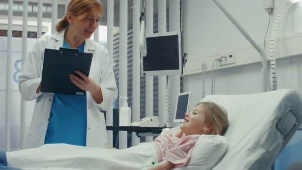 クリップボードとフレンドリーな医者 病院のベッドの上の少女嘘を回復 質問をします かわいい子は撮影のモダンな小児の看護 小児棟 — ストック動画