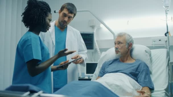 在医院里 躺在床上的老人 与用平板电脑诊断他的医生和护士交谈 技术帮助治疗病人 现代医院病房 — 图库视频影像