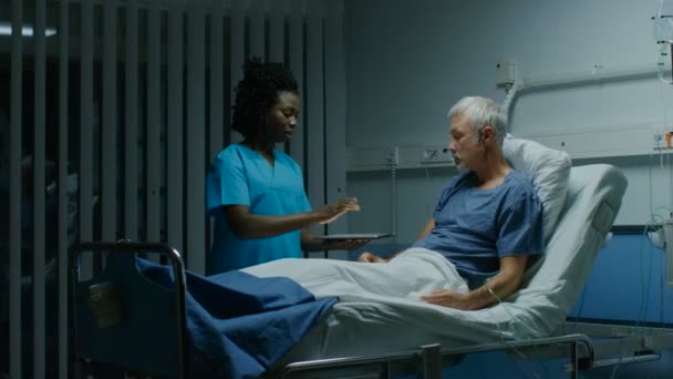 病院ベッド看護師持株タブレット コンピューターに横たわっている先輩患者実感情報を表示 身ぶりをする話 技術的に高度な病棟の — ストック動画