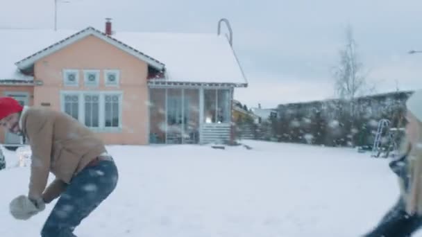 美しいカップルは お互いの間雪が降るで雪玉をスローします 幸せな男と女が彼らの牧歌的な家の庭に雪で遊んで 冬を楽しんでいる家族 — ストック動画