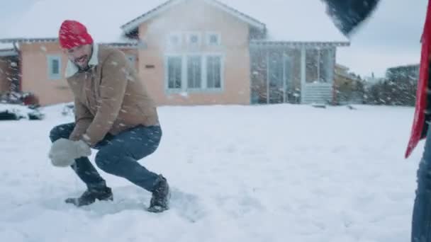 年轻美丽的情侣扔雪球在对方 而雪瀑布 快乐的男人和女人玩雪在院子里的田园诗般的房子 冬季享受的家庭 — 图库视频影像