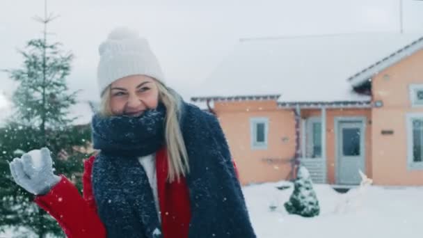 幸せな女性の若い笑顔雪だるまをスローと つでヒットを取得します 赤いコートの女の子は 彼女のパートナーと冬を楽しんでいます 牧歌的な家の裏庭での — ストック動画