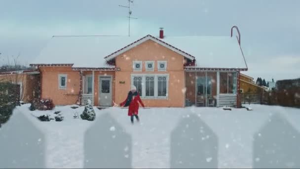 笑顔の美しい若い女性はジャンプし 雪でスピンします スカーフと赤いコートの女の子は 裏庭で冬の日を楽しんでいます バック グラウンドで立っている牧歌的な家 — ストック動画