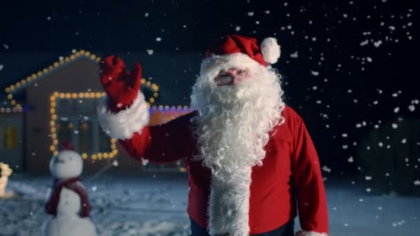 Portrét autentické Santa Claus, mávl rukou. Nový rok Eve Santa přináší radost, dárky a dárky pro každého. V pozadí domě ozdoben na Vánoce a padající sníh.