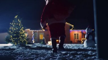 Otantik Noel Baba taşıyan kırmızı çanta over Shoulder, pastoral evi dekore Noel için dışarı yürür. Santa hediyeler ve Presents gece getiriyor. Büyülü New Year's Eve düşen kar.
