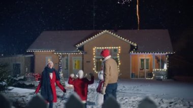 Mutlu yeni yıl kutlama, üç güzel havai fişek izlerken ön bahçesinde duran genç aile. Akşam kar sırasında düşen baba, anne ve küçük kızı sevimlisiniz hayretle doldu. Noel arifesi için çelenk ile dekore ev