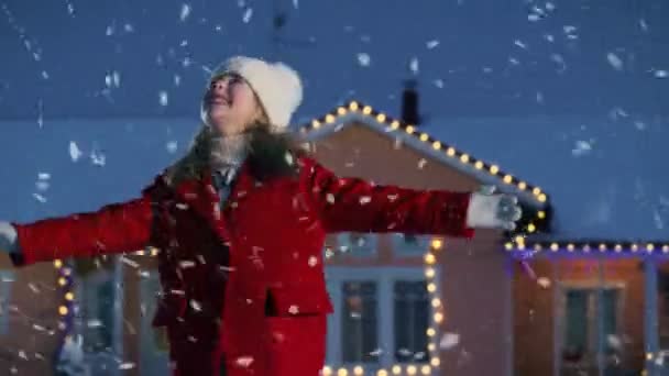 雪でかわいい小さな女の子踊り 子供は 冬の天気を楽しんでいます つの花輪 クリスマス ツリーで飾られた家のバック グラウンドでの冬の夜を楽しんでください — ストック動画