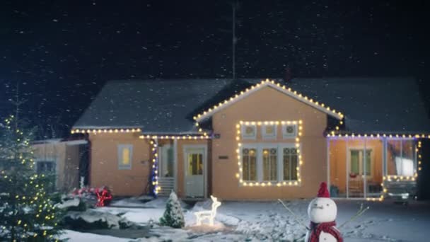 クリスマス 雪だるま クリスマス ツリーの花輪で飾られた牧歌的な家の映像は 裏庭に立っています 柔らかい雪に美しい冬の夜 — ストック動画