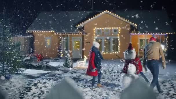 幸せな冬夜若い父 母とかわいい小さな娘を果たす雪玉 花輪で飾られた彼らの牧歌的な家の裏庭に彼らが作った雪だるまの周りを実行しています — ストック動画