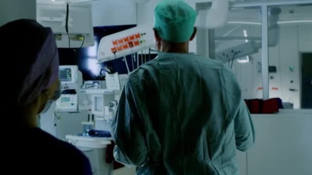 外科医とアシスタントの多様なチームのショットの後、患者が待つ手術室に入ると、彼らは麻酔の下に彼を置き、手術を開始します。本物の設備を備えた本物の近代的な病院. — ストック動画