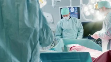 Muhtelif Profesyonel Cerrahlar Ekibi Hastane Ameliyathanesinde Bir Hastaya İstilacı Ameliyat Yapıyor. Cerrah Kullanımı ve diğer araçlar, Anestezi Uzmanı Hayati bulguları İzliyor.