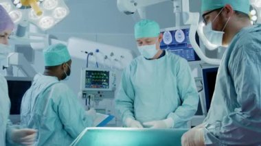 Muhtelif Profesyonel Cerrahlar Ekibi Hastane Ameliyathanesinde Bir Hastaya İstilacı Ameliyat Yapıyor. Hemşire aletleri cerrahlara dağıtıyor, anestezi uzmanı hayati organları izliyor. Modern Hastane.