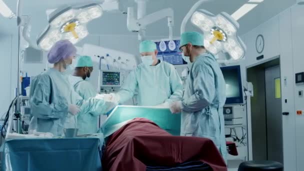 Olika team av professionella kirurger utför invasiv kirurgi på en patient i sjukhusets operationssal. Sjuksköterska Hands Out Instrument till kirurg, narkosläkare Övervakar värden. Modernt sjukhus. — Stockvideo