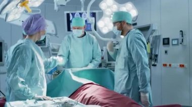 Profesyonel Cerrah, Asistanlar ve Hemşirelerden oluşan Yüksek Açı Çekimi Hastane Ameliyathanesinde İstilacı Ameliyat Yapıyor. Otantik Ekipmanlı Gerçek Modern Hastane.