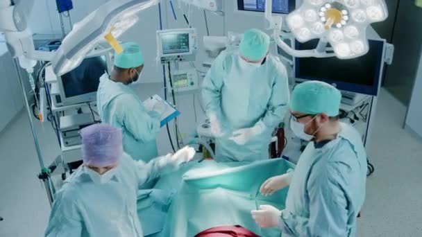 Équipe diversifiée de chirurgiens professionnels, d'adjoints et d'infirmières pratiquant une chirurgie invasive sur un patient dans la salle d'opération de l'hôpital. Les chirurgiens parlent et utilisent des instruments. Véritable hôpital moderne avec équipement authentique . — Video