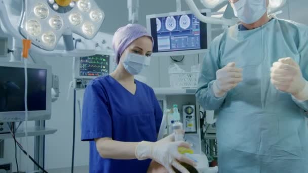 Dans la salle d'opération de l'hôpital, l'anesthésiste applique un masque d'anesthésie à un patient, les assistants désinfectent avec de l'iode lieu d'incision, les chirurgiens attendent pour commencer la chirurgie. — Video