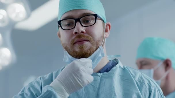 In het ziekenhuis operatiekamer professionele chirurg zet op chirurgische masker en bochten rond en sluit zich aan bij andere artsen in chirurgie. — Stockvideo