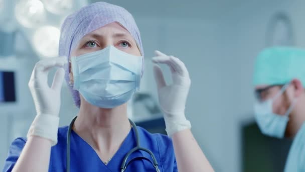 Retrato de la enfermera profesional / asistente médico quitándose la máscara quirúrgica después de una operación exitosa. En el fondo Moderno quirófano del hospital. — Vídeos de Stock