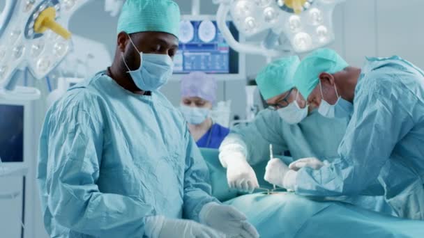 Professional Surgeon Standing in Surgical Mask Arms Crossed. In the Background Modern Hospital Operating Room with Surgery in Progress. — Stock Video