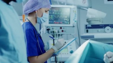 Hastane Ameliyathane anestezist Görünüyor ve Monitörler ve Kontroller Hastanın Hayati Belirtileri, Cerrahi devam etmek için bir BaşHekim başını sallayarak.