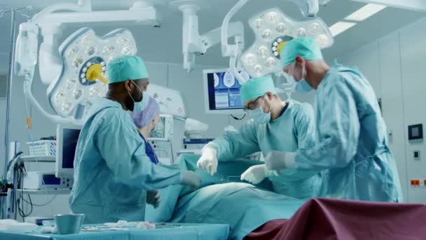 Professzionális sebészek sokszínű csapata, akik invazív műtétet végeznek egy betegen a kórház műtőjében. Sebészek használata és egyéb eszközök. — Stock videók