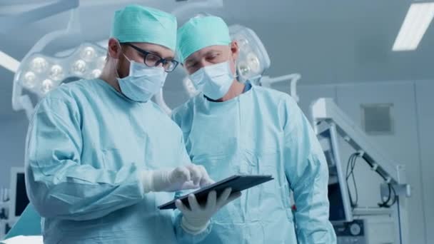 2つの専門外科医は、現代の病院の手術室に立っている間、デジタルタブレットコンピュータを使用します. — ストック動画