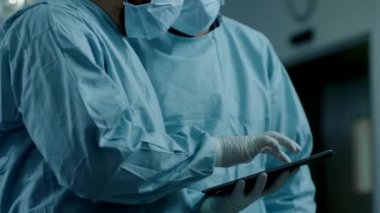 Modern Hastane Ameliyat Odası 'nda dururken iki profesyonel cerrah dijital tablet bilgisayar kullanıyor..