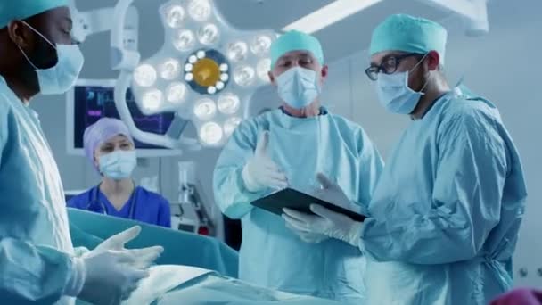 Professionele chirurgen en assistenten praten en gebruiken digitale tablet computer tijdens chirurgie. Ze werken in de operatiekamer van het moderne ziekenhuis. — Stockvideo