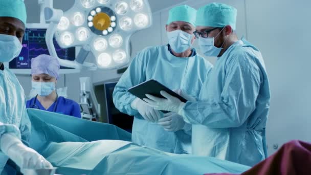 Professionella kirurger och assistenter prata och använda digital surfplatta dator under operation. De arbetar i det moderna sjukhusets operationssal. — Stockvideo