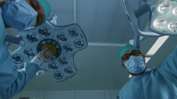 Vista del paciente de POV de tiro en ángulo bajo: dos cirujanos profesionales encienden luces de cirugía mientras se inclinan sobre el paciente. — Vídeos de Stock