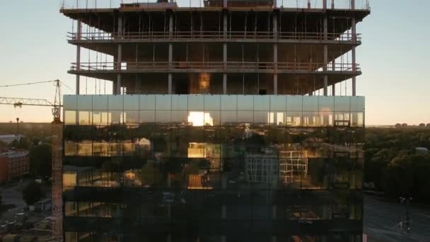 Luchtfoto van het wolkenkrabber gebouw in het bouwproces. In de achtergrond werkende kraan, bos, zee en zonsondergang. — Stockvideo