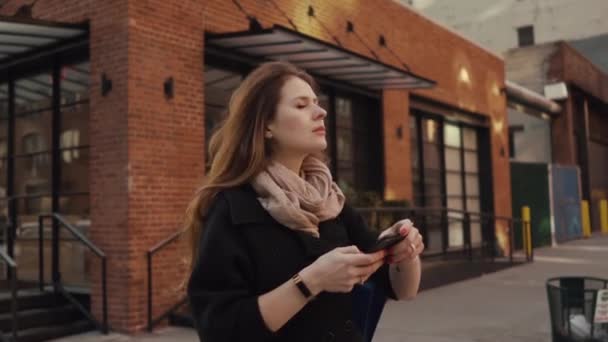 Hermosa chica pelirroja en una prisa en Big City, utiliza Smartphone. Esperando a un amigo o perdido . — Vídeos de Stock