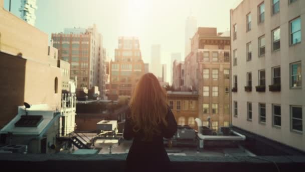 Back View shot van mooie roodharige vrouw staande op een dak. Stedelijk stadsgezicht uitzicht op New York City met grote wolkenkrabbers en gebouwen. — Stockvideo