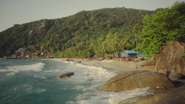 Bella vista su una spiaggia con onda sul mare, villaggio sulla riva e lussureggiante giungla verde sullo sfondo . — Video Stock