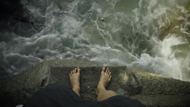 Hög vinkel skott av personens ben stående på en klippa nära havet med sopor och skräp flytande nära stranden. — Stockvideo