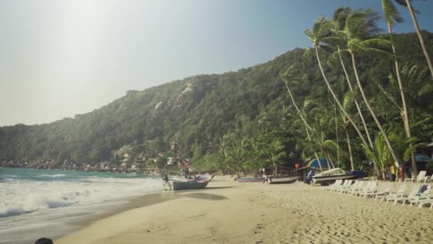 Bewegende Aufnahme an einem idyllischen Strand mit Wellen und Meer, Booten an Land und im Hintergrund Hügel mit grünem Dschungel. — Stockvideo