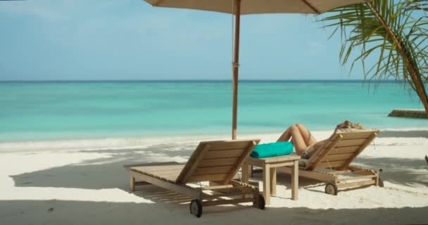 Primer plano de la hermosa rubia acostada en la silla de cubierta en la playa. Tomar el sol en la ubicación exótica con el mar turquesa en el fondo . — Vídeos de Stock