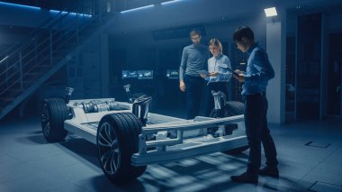 Elektrikli araba platformu şasi prototip üzerinde çalışırken konuşan çeşitli otomobil mühendisleri. Otomotiv yenilik tesisi konsept araç çerçevesi lastikler, süspansiyon, motor ve pil Içerir