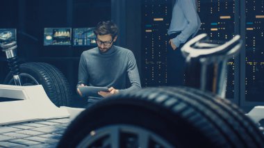 Otomobil Tasarım Mühendisi oturma yanında Hybrid elektrikli araba şasi platform prototip, kullanma tablet bilgisayar için tasarım geliştirme. Süspansiyon, jantlar, motor ve pil ile araç çerçevesi ile tesis