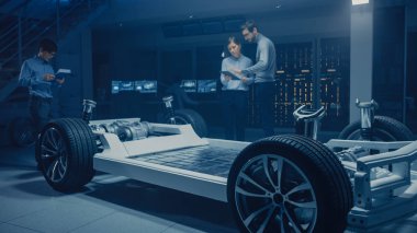 Elektrikli araba platformu şasi prototip üzerinde çalışırken konuşan çeşitli otomobil mühendisleri. Otomotiv yenilik tesisi konsept araç çerçevesi lastikler, süspansiyon, motor ve pil Içerir