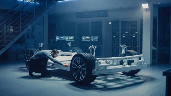 Ingénieur automobile travaillant sur le prototype de châssis de plate-forme de voiture électrique, utilisant un ordinateur tablette avec modélisation logicielle CAO 3D. Installation innovante : Cadre de véhicule avec roues, moteur, batterie et suspension — Photo