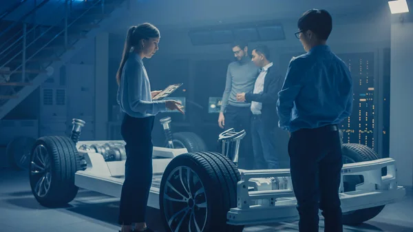 Automobilové inženýři diskutují a navrhují platformu elektromobilu, používání počítačů Tablet s 3D CAD softwarem. Rám vozidla pro inovace automobilů s koly, motorem a baterií — Stock fotografie