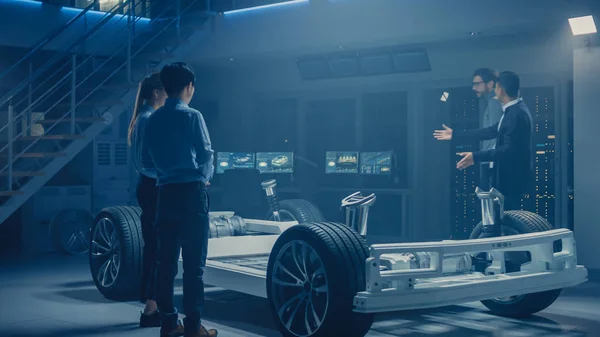 Auton insinöörit keskustelevat ja suunnittelevat Electric Car alustan, käyttäen Tablet-tietokoneita 3D CAD-ohjelmistolla. Automotive Innovation Facility ajoneuvon runko pyörillä, moottorilla ja akulla — kuvapankkivalokuva