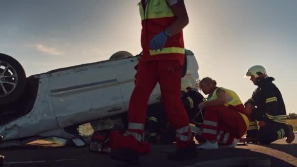 Sulla scena degli incidenti stradali: squadra di paramedici e vigili del fuoco soccorritori feriti intrappolati nel veicolo ribaltabile. Professionisti vittime estrinsecate, dare il primo soccorso, spegnere il fuoco — Video Stock