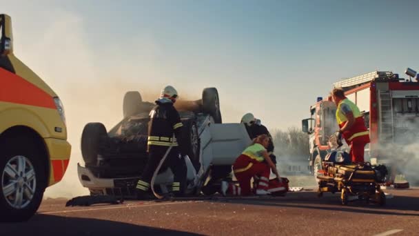 Sulla scena dell'incidente stradale: paramedici e vigili del fuoco soccorrono le vittime ferite intrappolate nel veicolo. I medici usano le barelle, eseguono il pronto soccorso. Pompieri afferrare attrezzature da Fire Engine — Video Stock