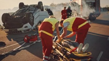 Araba kazasında trafik kaza sahnesinde: sağlık görevlileri küçük bir kız sedye üzerinde yatan hayat tasarruf, o Ilk yardım yardımı verildi. İtfaiyeciler annesini kızına götürür. Arka planda rollover araç