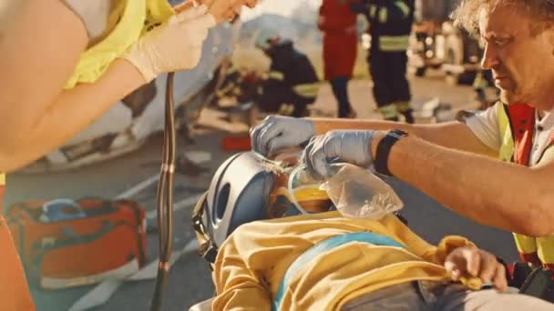 Na místě dopravní nehody: záchranáři zachraňují život oběti dopravní nehody, která leží na nosítkách. Poslouchají tlukot srdce, aplikovat kyslíkovou masku a poskytnout první pomoc — Stock video